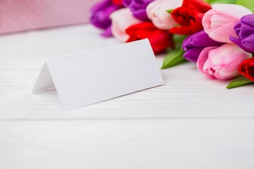 Folded tent card is standing on wooden tabletop, showing flat design with tulip bouquet, copy space