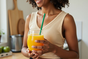 A woman holding a glass of orange juice with a green straw.