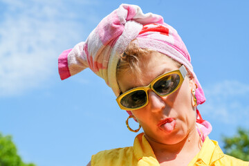 Junge Frau mit Badetuch um den Kopf und goldener Sonnenbrille hat Spass und zieht Grimassen