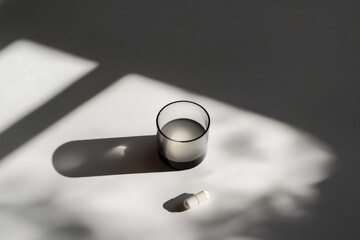 glass tumbler and pills on grey background with shadow, treatment concept, dietary supplements. copy space 