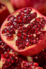 Close-up of a sliced pomegranate revealing juicy red seeds. The fruit has a vibrant red exterior and a textured surface, showcasing its natural beauty.