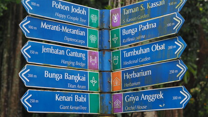 A close-up of a colorful multi-directional signpost in a tropical botanical park, pointing to various attractions, gardens, and themed areas © Ruud