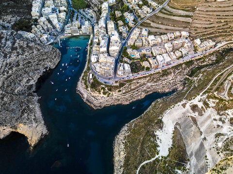 Aerial view of azure waters embrace rugged cliffs and quaint buildings in a captivating coastal panorama, Munxar, Munxar, Malta.