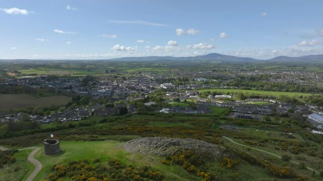 Vinegar Hill, Enniscorthy, County Wexford, Ireland, April 2025. Drone slow pullback and ascend above rocks and stone tower monument overlooking nearby town, panoramic view to horizon.
