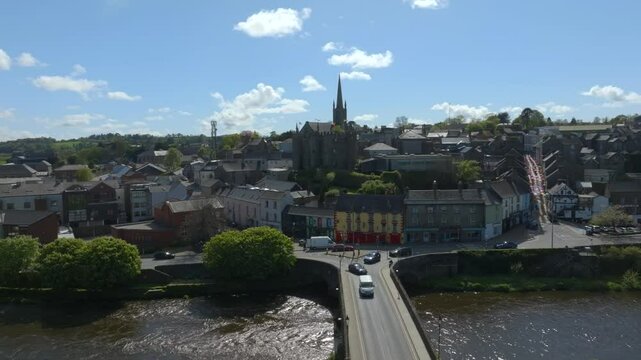 Enniscorthy, County Wexford, Ireland, April 2025. Drone starts from static over bridge leading to castle orbits counter clockwise to establish village with towers and iconic spires on sunny day.