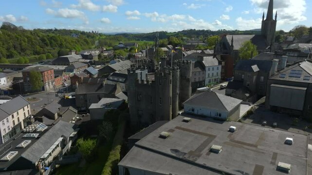 Enniscorthy Castle, County Wexford, Ireland, April 2025. Drone orbits counterclockwise of Norman castle flying Irish flags swaying in the wind as birds soar around in sky, establishing overview.