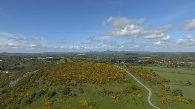 Vinegar Hill, Enniscorthy, County Wexford, Ireland, April 2025. Drone panoramic aerial approach with stone tower monument on left third pushing forward to reveal parking lot and town.