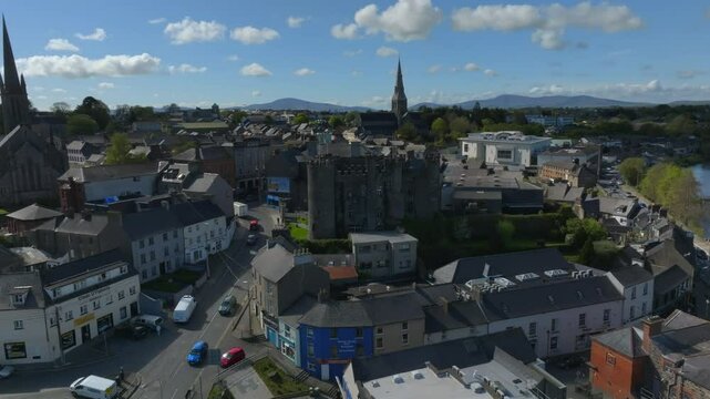 Enniscorthy Castle, County Wexford, Ireland, April 2025. Drone slow pullback keeping historical monument centered as cars drive by up hill below storefronts on a sunny day.