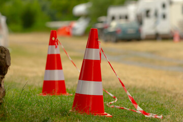 Two bright red and white traffic cones are prominently sitting in a patch of green grass, creating...