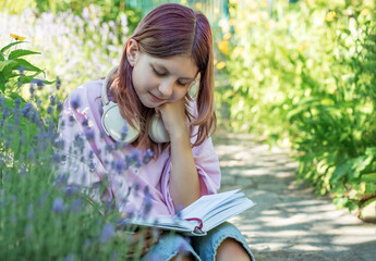 Young student reading a book while listening to music in a garden