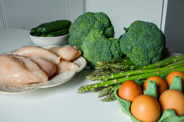 Raw chicken fillet, eggs and green veggies on white table