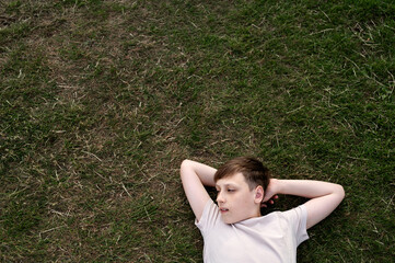 Teen boy relaxing on grass with his hands behind his head.