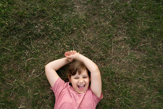 Laughing child girl with arms crossed behind head lying on the grass.