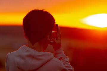 A man is capturing a beautiful picture of the sunset scene using his cell phone, making sure to...