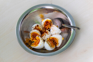 Healthy soft boiled eggs, cut in half in a steel bowl, ready to eat with a spoon on wood. Spiced...