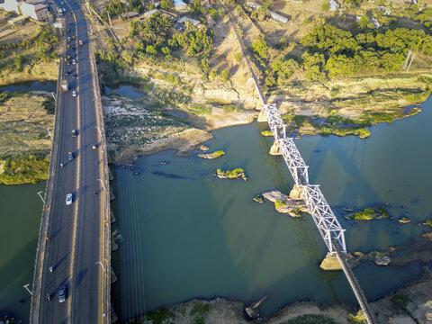 Aerial View of parallel bridges span the vibrant, winding river, juxtaposed against the arid landscape where the green of the river meets the brown earth, Kaduna, Kaduna, Nigeria