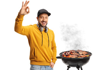 Young man with headphones gesturing ok sign in front of a bbq