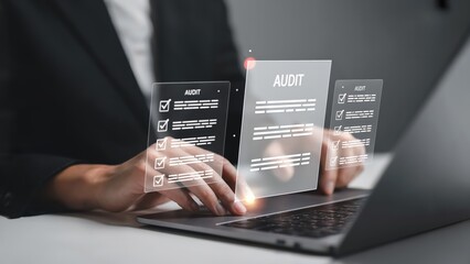 Business professional reviews audit documents on a modern laptop computer.