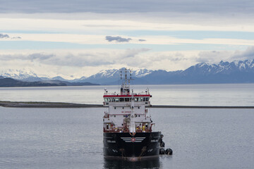 Punta Arenas, Chile - 12 June 2025: Aerial view of a sturdy ship slicing through the calm, steely waters, framed against a backdrop of snow-capped mountains under a hazy sky.