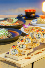 Japanese Fusion Dinner by the Sea, A beautifully arranged seafood dinner featuring sushi rolls, grilled fish, and dipping sauce, set against a peaceful seaside backdrop at night.