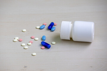 Assorted tablets, capsules, and pills scattered on the floor with a fallen medicine bottle nearby....