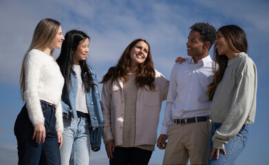 Five young mutiethnic friends sharing ideas and smiling under blue sky