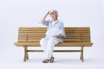 Elderly Woman sitting on a bench, suffering from the heat while fanning himself. Concept of  global...