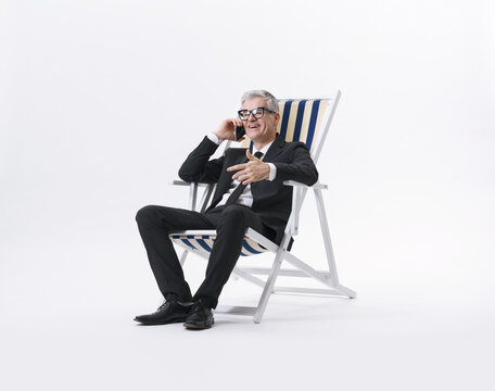 Manager in a black suit talking on the phone while sitting on a beach chair, isolated on a neutral background