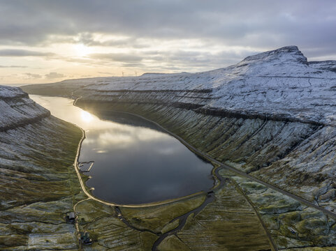 Aerial view of a serene lake nestled between snow-dusted mountains, reflecting the soft, golden light of the setting sun, Tj&Atilde;&cedil;rnuv&Atilde;&shy;k, Streymoy, Faroe Islands.
