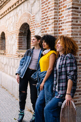 Three young friends, two girls and a boy, with inline skates and skateboards, are leaning against a...