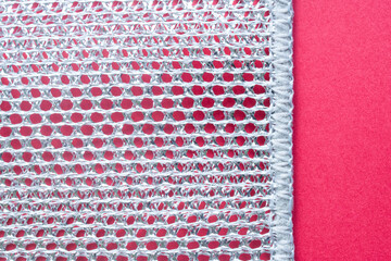 Macro shot highlights the abstract texture of a cleaning sponge, with a striking contrast between metallic and red hues. Photo. High resolution.
