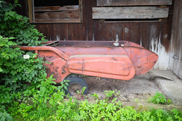 A rusty red wheelbarrow is sitting in a field of green grass