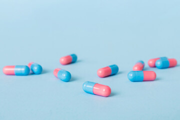 Heap of pink and blue pills on colored background. Tablets scattered on a table. Pile of red soft gelatin capsule. Vitamins and dietary supplements concept