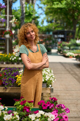 Confident female gardener posing with crossed arms in plant nursery