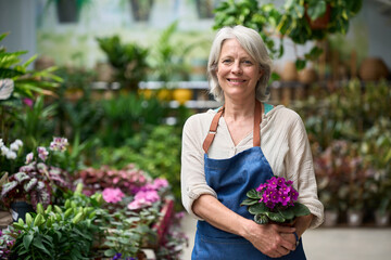 Senior woman working in a greenhouse holding a potted plant
