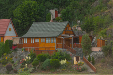 A charming house that features a green roof is positioned atop a gentle hill, beautifully surrounded by tall trees that provide shade and character