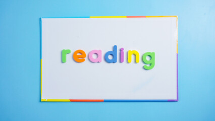 Colorful letters spelling word READING on whiteboard isolated on blue background