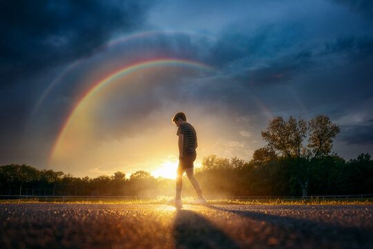Pre-teen Boy Walking Under Storm Clouds with Rainbow