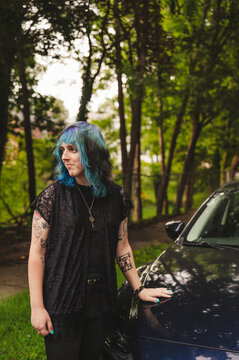 Transwoman with dyed hair standing outdoors by a car