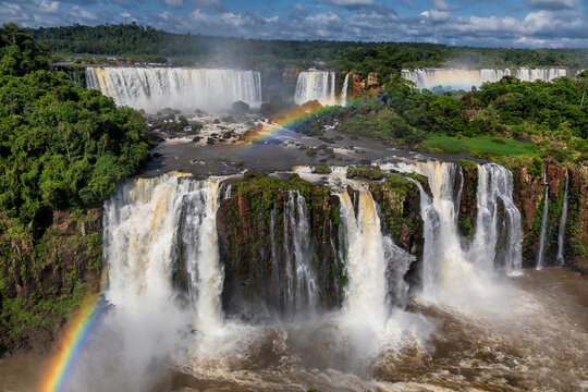 View of majestic waterfalls cascading down rocky cliffs amidst lush greenery, with vibrant rainbows painting the mist in Iguaz&Atilde;&ordm;, Ciudad Aut&Atilde;&sup3;noma de Buenos Aires, Argentina.