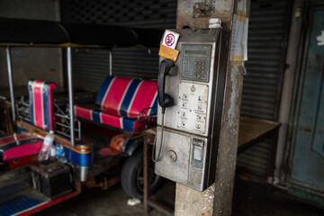 An old metal coin-insert public phone hanging on a column outside a store
