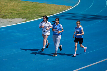 Teenage girls running on blue track at athletics competition