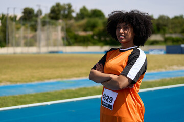 Confident female athlete posing on running track with arms crossed
