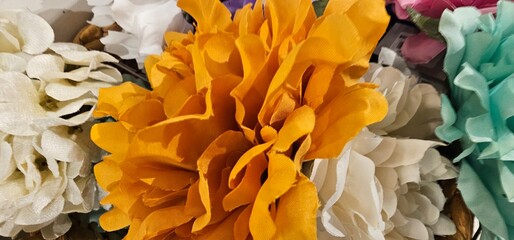 Bright artificial orange flower with soft ruffled petals, surrounded by white, aqua, and pink fabric flowers in a close-up arrangement. artificial flower, orange;