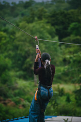 Young woman ziplining, enjoying adventurous activity amidst lush green Indian landscape.