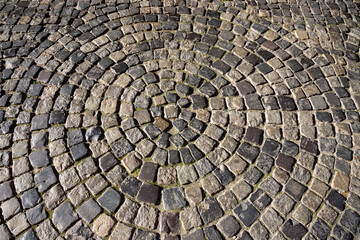Circular pattern of cobblestone pavement in a public square surrounded by greenery and historic architecture during bright daylight © Oleh Marchak