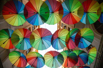Fototapeta premium Colorful umbrellas decorate narrow alleyway in vibrant display during a sunny day in a lively urban area