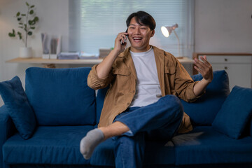 A man is sitting on a blue couch and talking on his cell phone