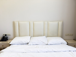 A white bed with a phone on the nightstand. There are three white pillows on the bed