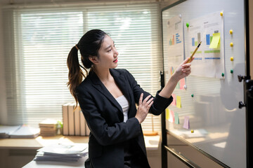 A woman in a black suit is pointing at a white board with a green marker